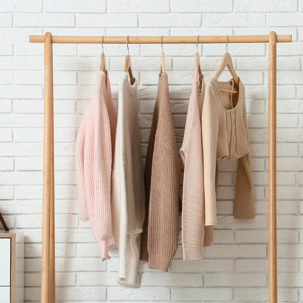 Five sleeveless tops hanging on a wooden rack against a white brick wall.